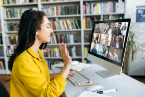 Online education. A female student learning online at home, she waving hand to other students or colleagues on computer monitor in video conference and smiling
